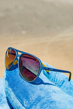 Óculos de sol SPORTBR Goodr Frequent SkyMall Shoppers com armação azul, lentes marrons polarizadas e hastes amarelas.