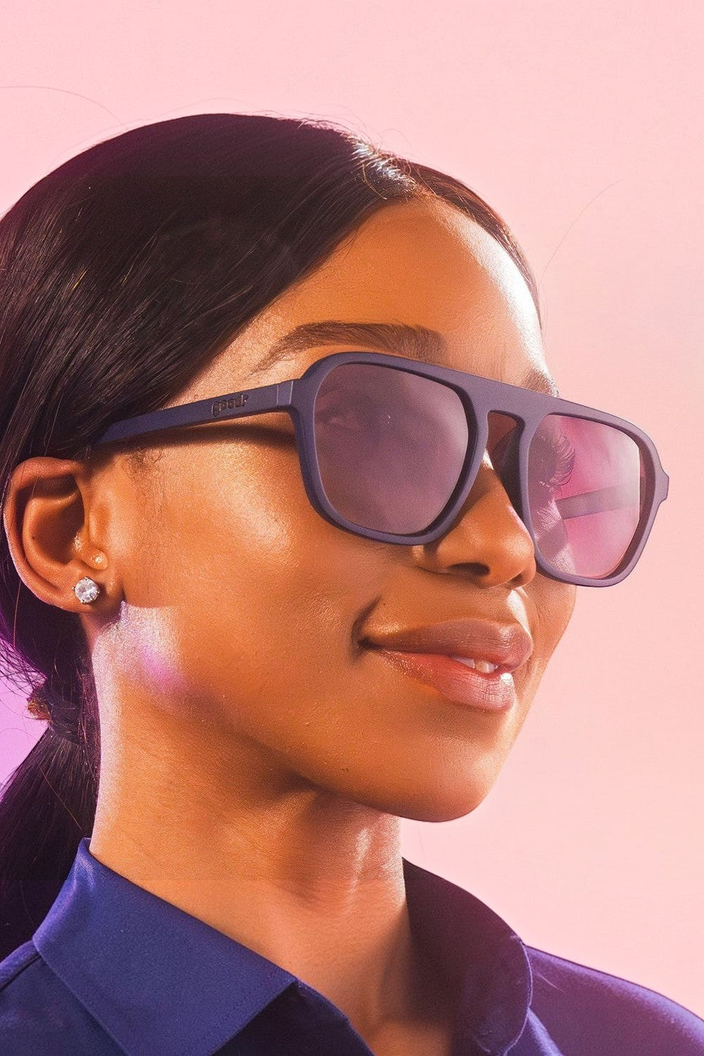 Modelo usando óculos de sol SPORTBR Goodr Deja Vu Daydream com armação azul escura e lentes roxas polarizadas.