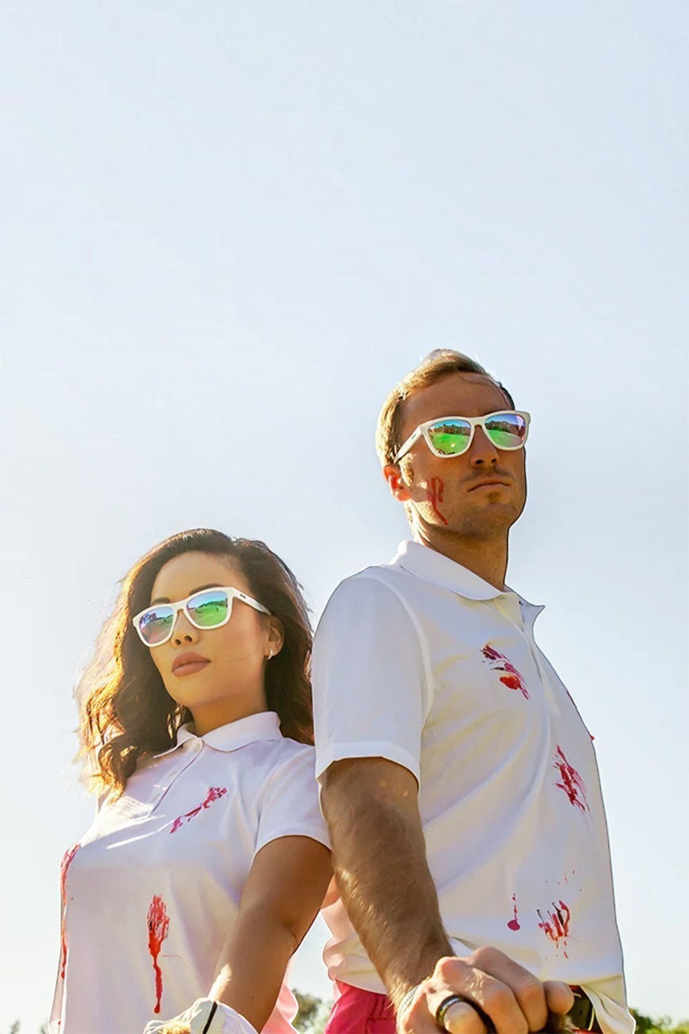 Homem e mulher usando óculos de sol Goodr brancos com lentes rosas em um dia ensolarado, vendidos pela SPORTBR.
