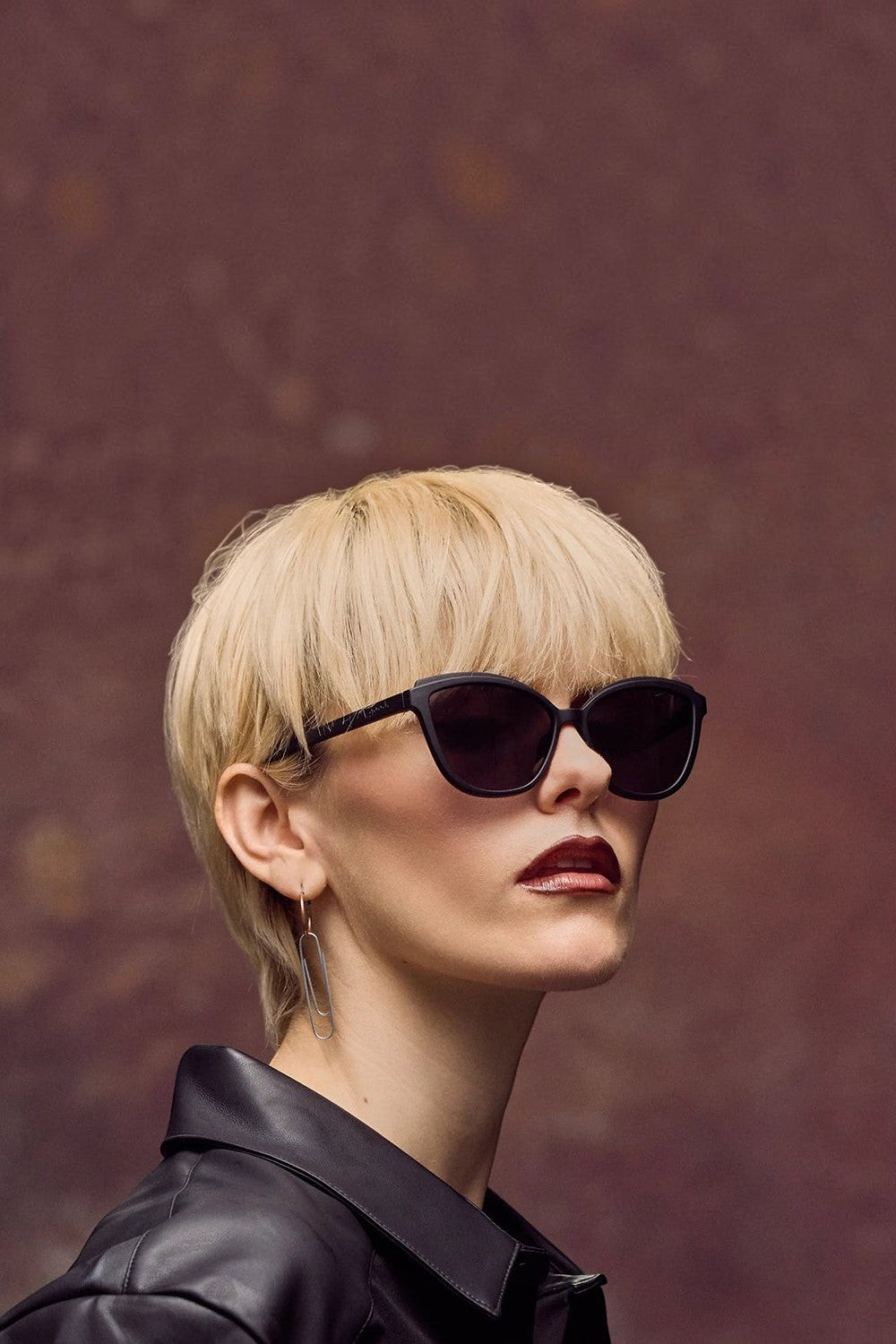 Modelo loira usando óculos de sol SPORTBR Goodr Not a Carbon Copy com armação preta estilo cat-eye e lentes escuras.