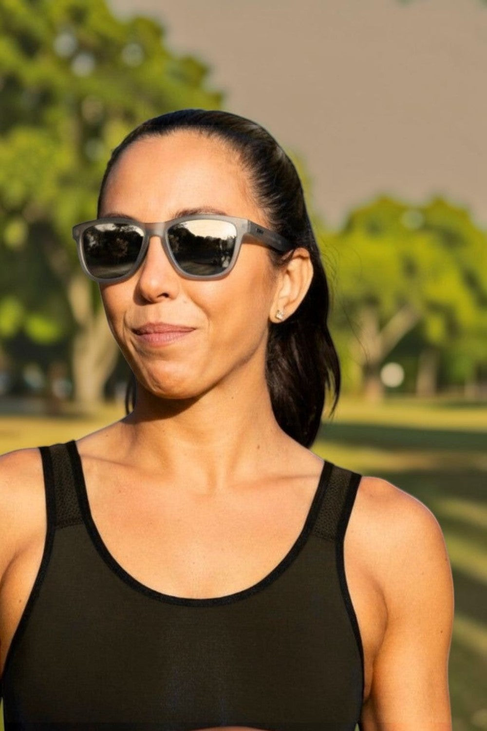 Mulher usando óculos de sol esportivos cinza Goodr Going to Valhalla Witness com lentes espelhadas na SPORTBR