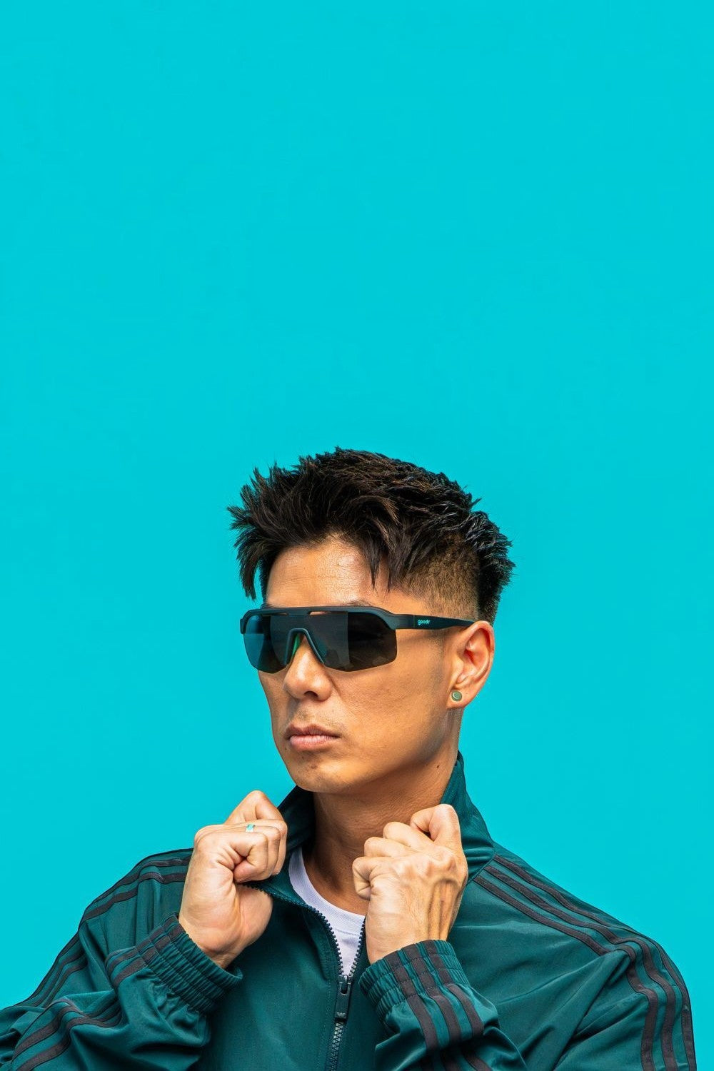 Homem usando óculos de sol SPORTBR Goodr Electric Zen Machine com armação verde azulada e lentes polarizadas verdes.