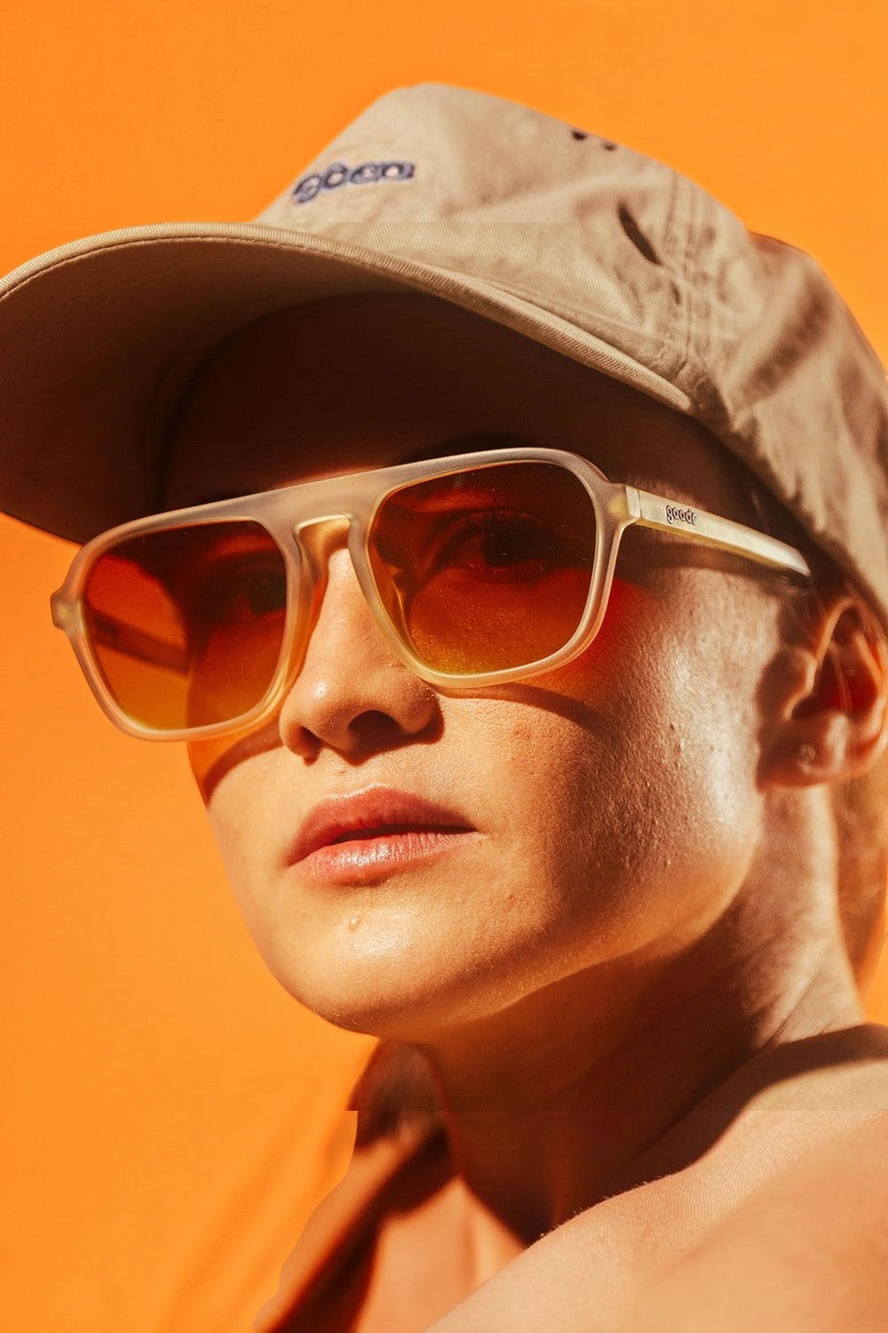 Pessoa usando óculos de sol SPORTBR Goodr Impromptu Disco Nap com armação cinza e lentes laranja em fundo alaranjado