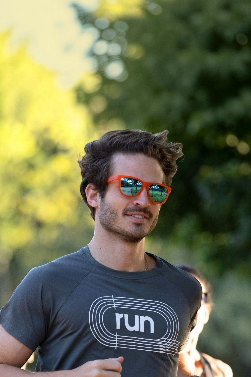Homem correndo ao ar livre usando óculos de sol SPORTBR Goodr Donkey Goggles com armação laranja e lentes espelhadas