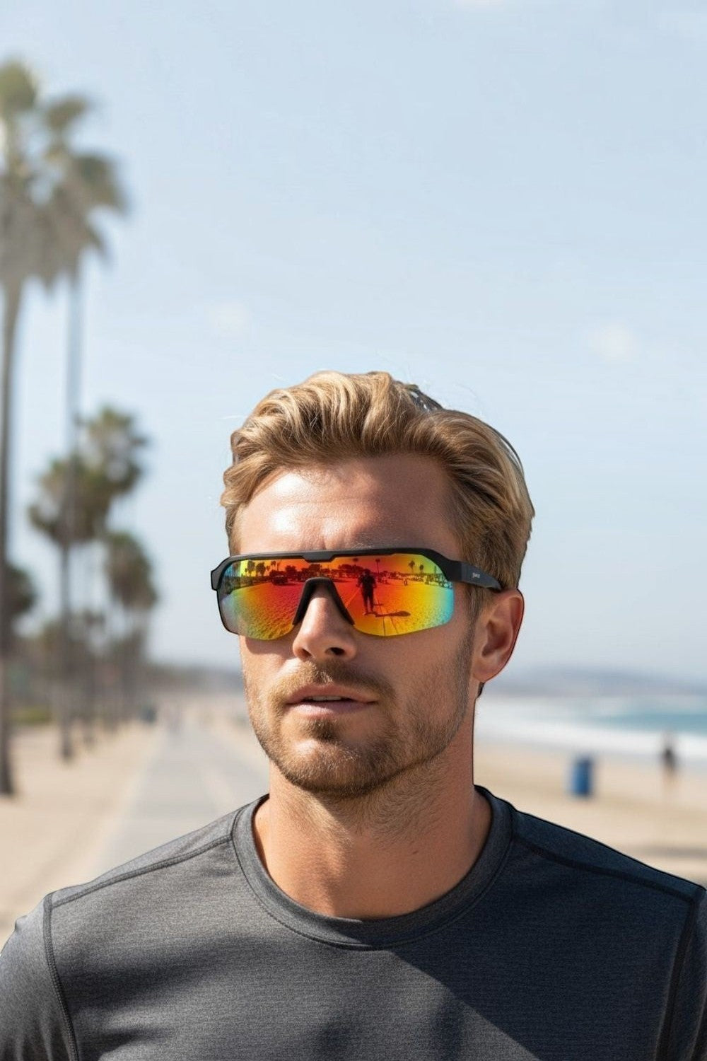 Homem usando óculos de sol SPORTBR Goodr com armação preta e lentes espelhadas laranja em um dia ensolarado na praia.