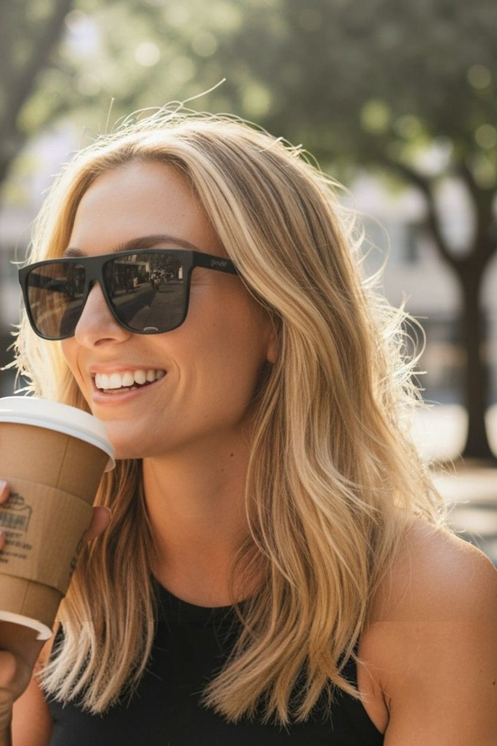 Mulher loira sorrindo usando óculos de sol SPORTBR Goodr Fashion Week Dropout pretos com lentes polarizadas