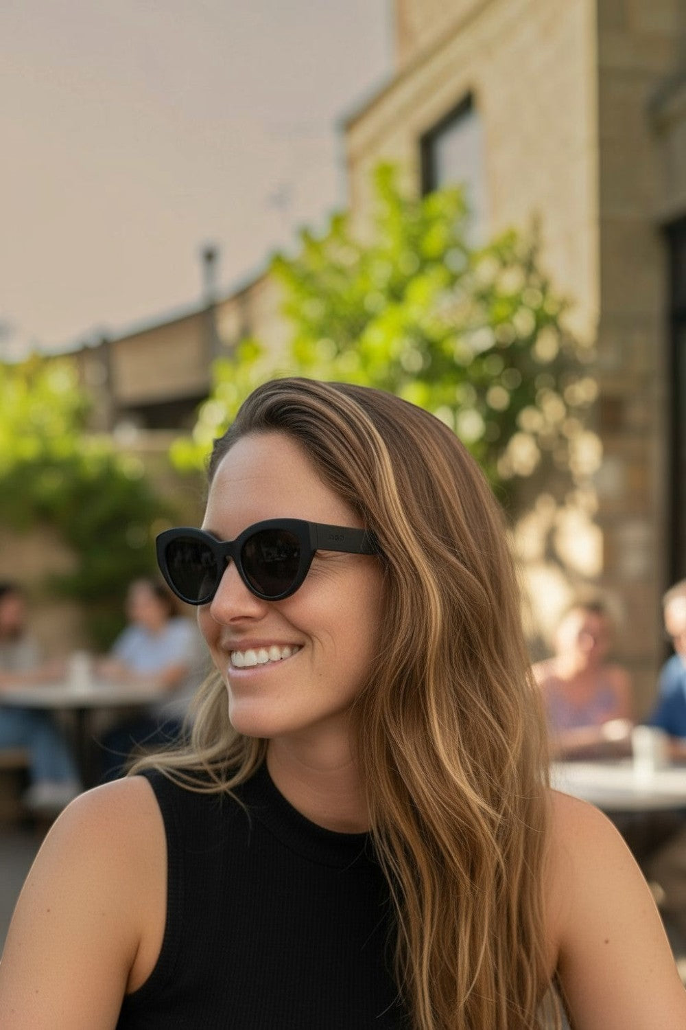 Mulher sorridente usando óculos de sol pretos SPORTBR Goodr In My Cosmic Era com lentes polarizadas em ambiente externo.