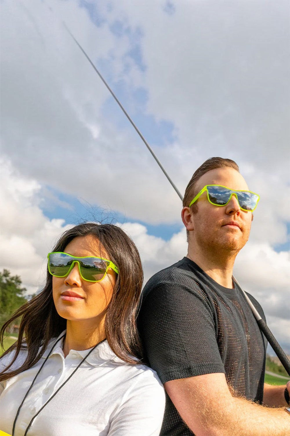 Homem e mulher usando óculos de sol SPORTBR Goodr Naeon Flux Capacitor com armação verde e lentes espelhadas