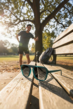 Óculos de sol esportivos SPORTBR Goodr Lava Lamp Oracle verdes com lentes polarizadas em banco de parque ao ar livre