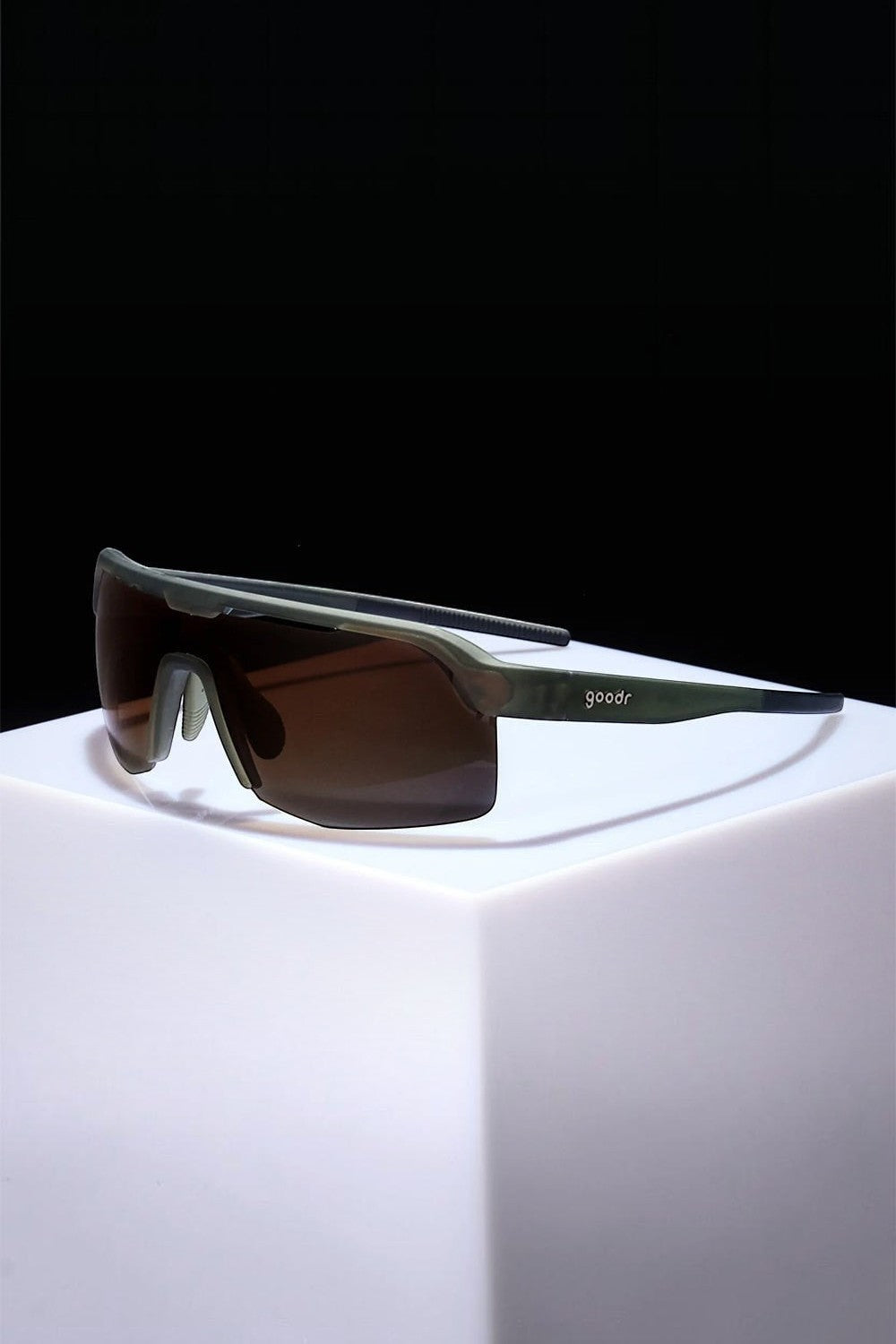 Óculos de sol SPORTBR Goodr verde com lentes âmbar, modelo esportivo polarizado para corrida sobre base branca.