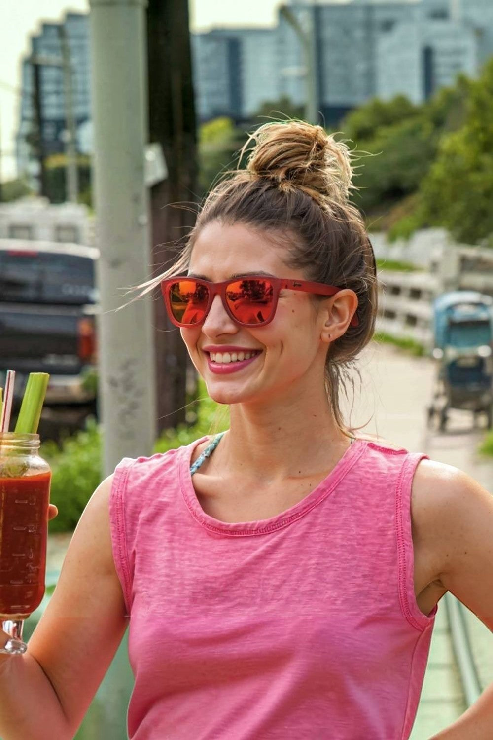Mulher usando óculos de sol esportivos SPORTBR Goodr vermelhos com lentes espelhadas rosas em ambiente externo