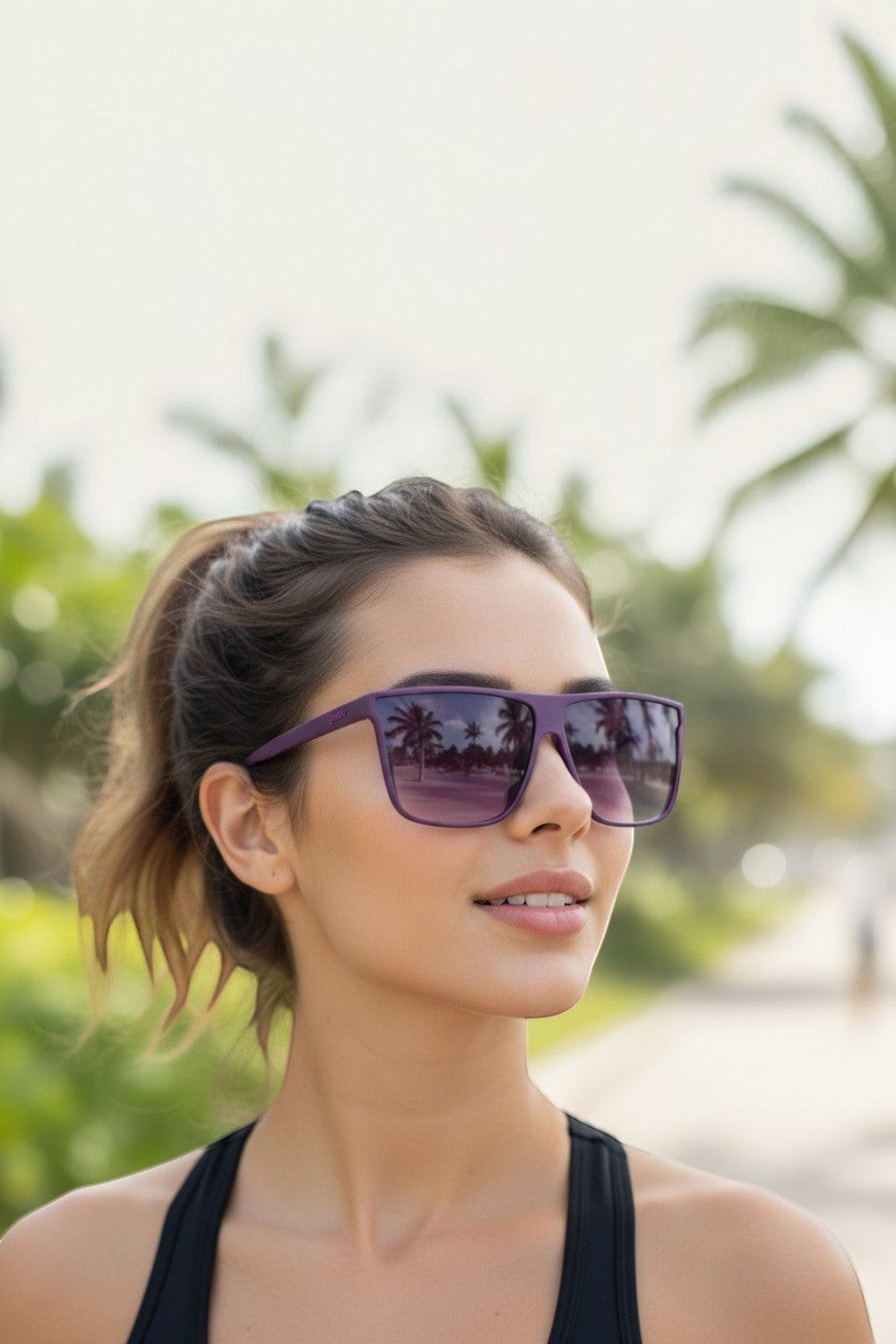 Mulher usando óculos de sol SPORTBR Goodr roxos com lentes polarizadas em ambiente externo ensolarado.
