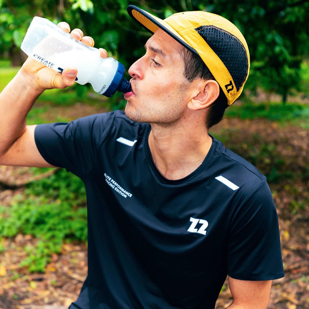 Homem bebendo água de uma garrafa, usando camiseta preta e boné amarelo da SPORTBR.