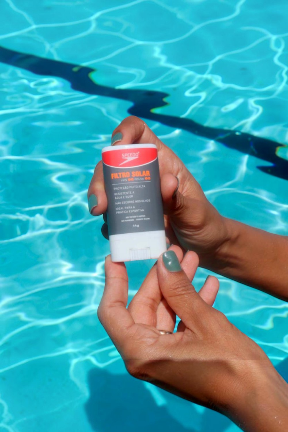 Protetor solar facial SPORTBR Speedo Pink Cheeks em bastão sendo segurado sobre uma piscina azul