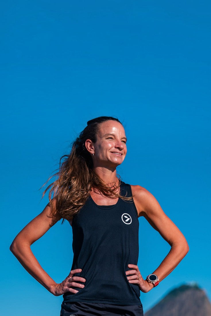 Mulher sorridente vestindo regata preta de poliamida SPORTBR Pace para corrida ao ar livre com céu azul ao fundo