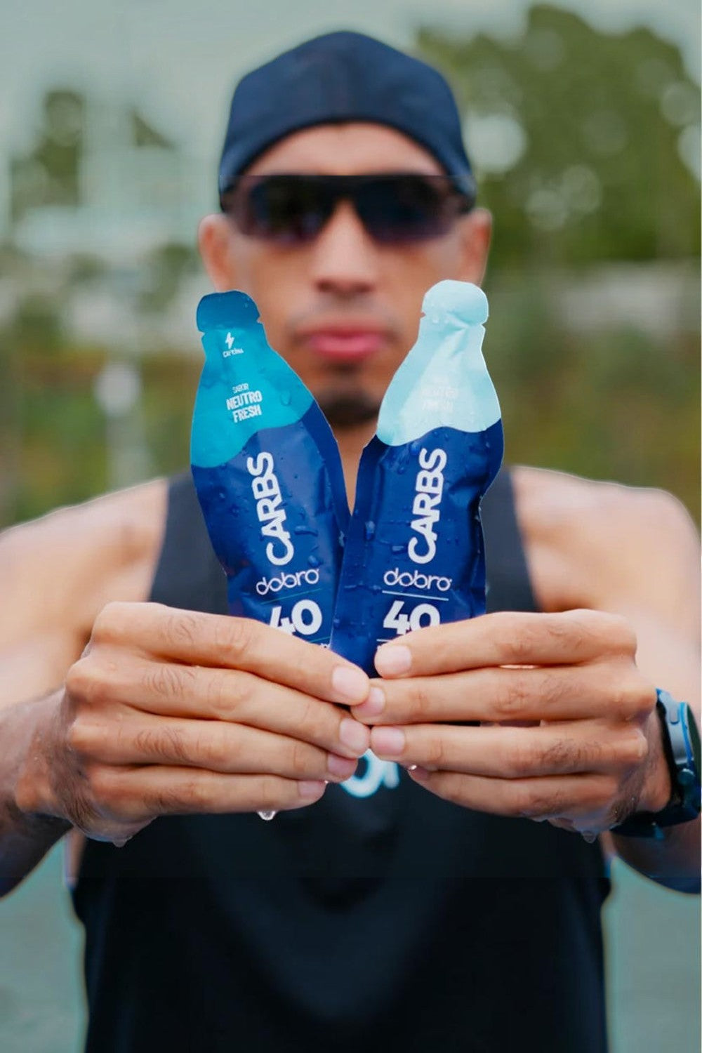 Atleta segurando dois sachês de gel de carboidrato SPORTBR Carbs 40 Dobro sabor Neutro Fresh com cafeína