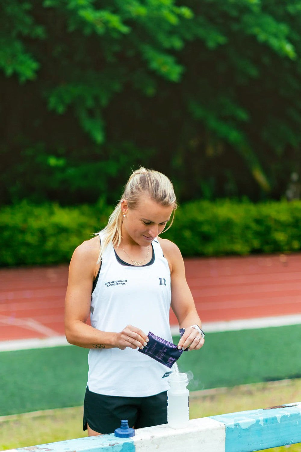 Atleta SPORTBR despejando sachê de Power Powder Z2+ sabor Grape Express em garrafa de água em pista de atletismo