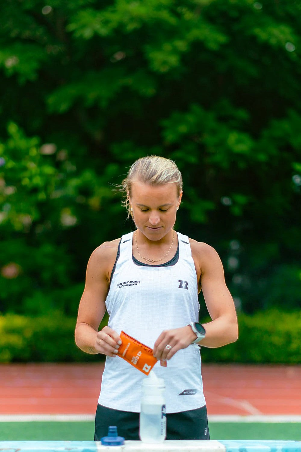 Atleta SPORTBR preparando sachê de Z2 Power Powder sabor Iced Tangerine em pista de corrida ao ar livre