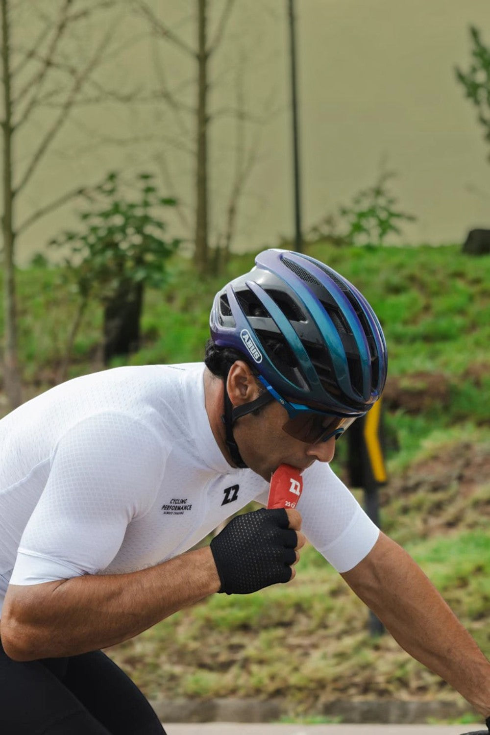 Ciclista SPORTBR usando capacete e camisa branca consumindo sachê de gel de carboidrato Z2 sabor Berry Sundae