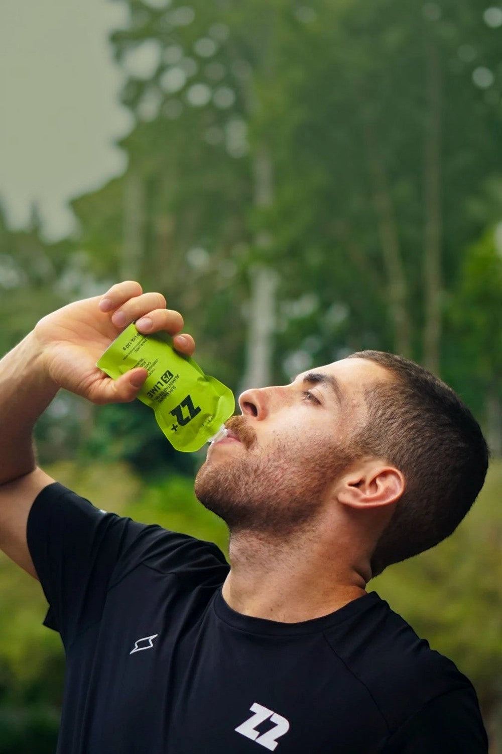 Atleta SPORTBR consumindo sachê de gel de carboidrato Z2+ sabor limão em embalagem flask verde durante treino ao ar livre.