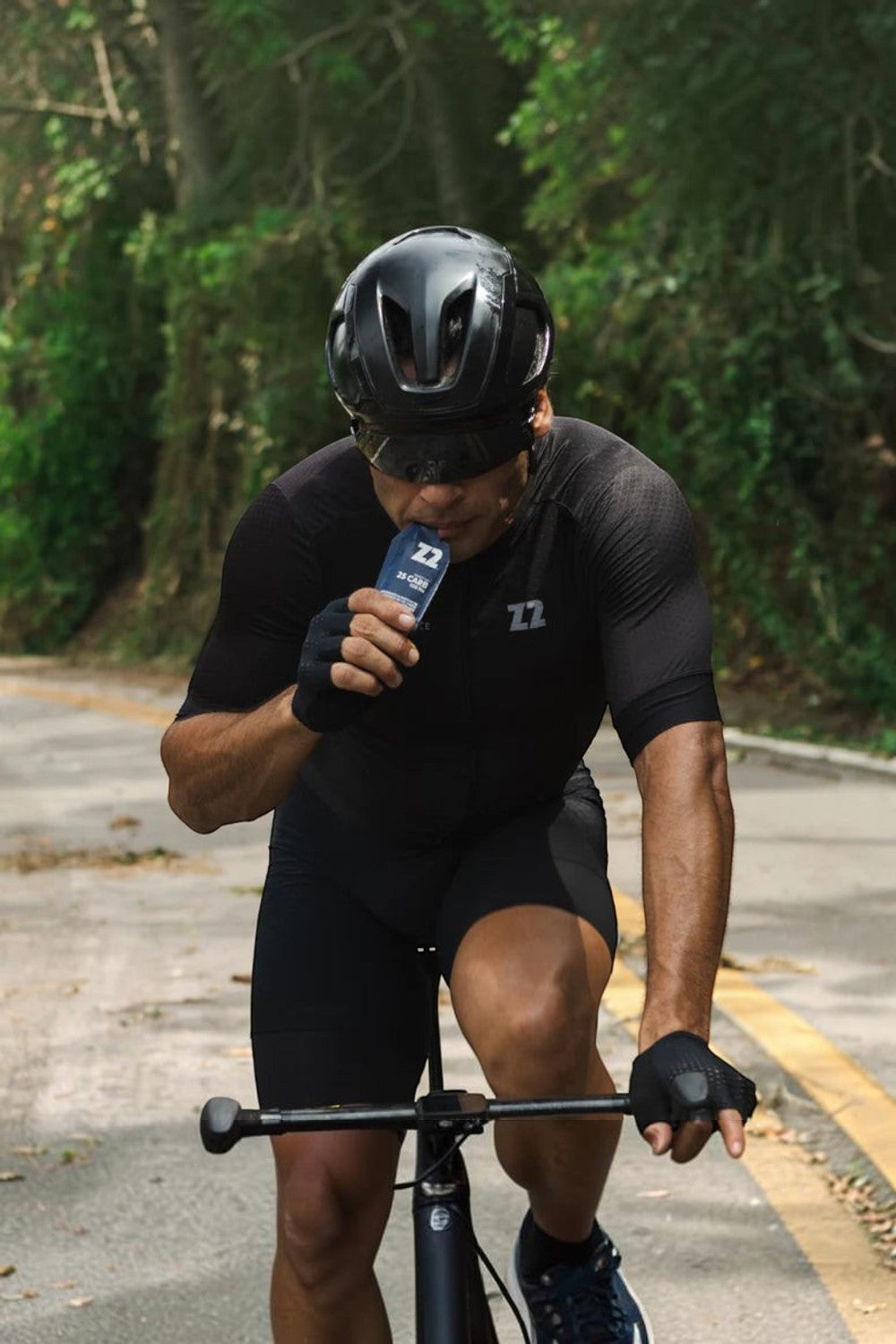 Ciclista SPORTBR usando capacete preto consumindo sachê de gel de carboidrato Z2 Tropical Fruit durante treino na estrada