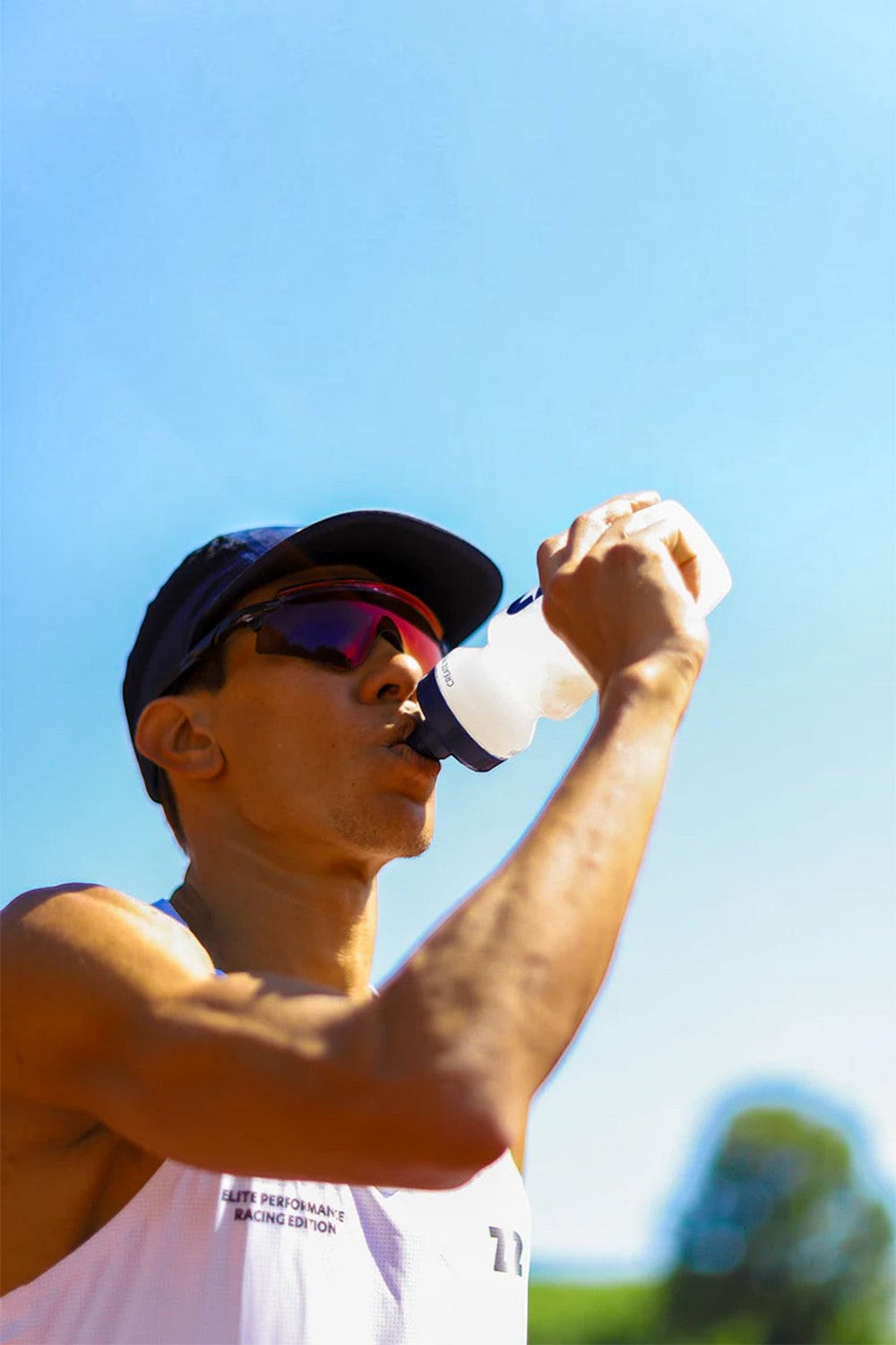 Atleta da SPORTBR bebendo isotônico Saltz 500 Z2 sabor frutas vermelhas durante treino ao ar livre sob sol forte