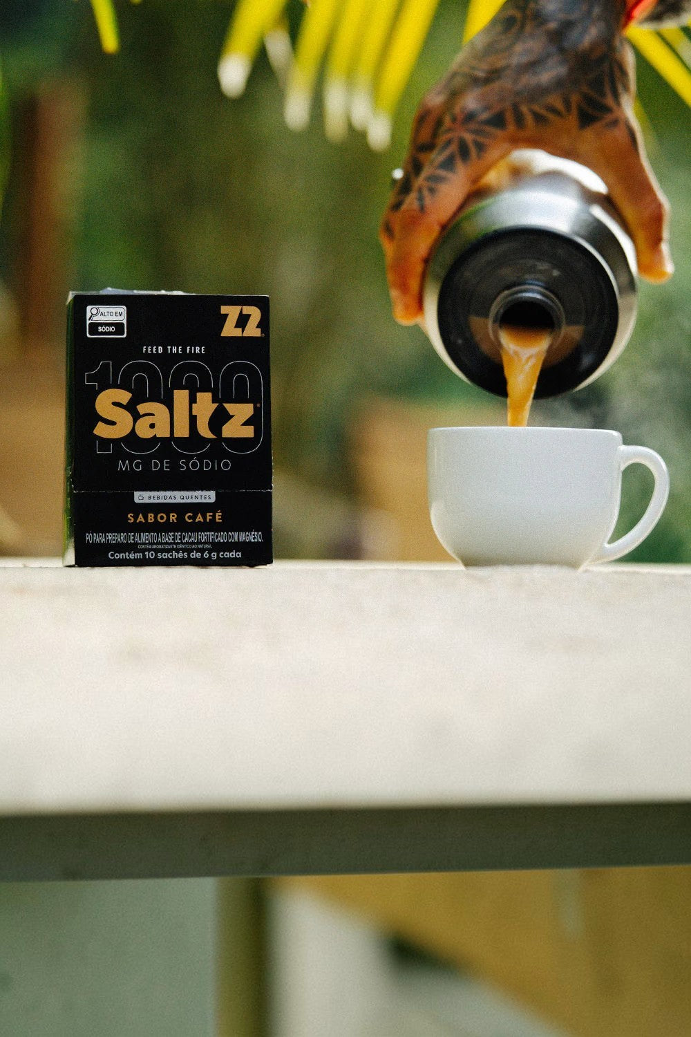 Sachê de eletrólitos SPORTBR Saltz Z2 sabor café sendo servido em uma xícara em ambiente externo