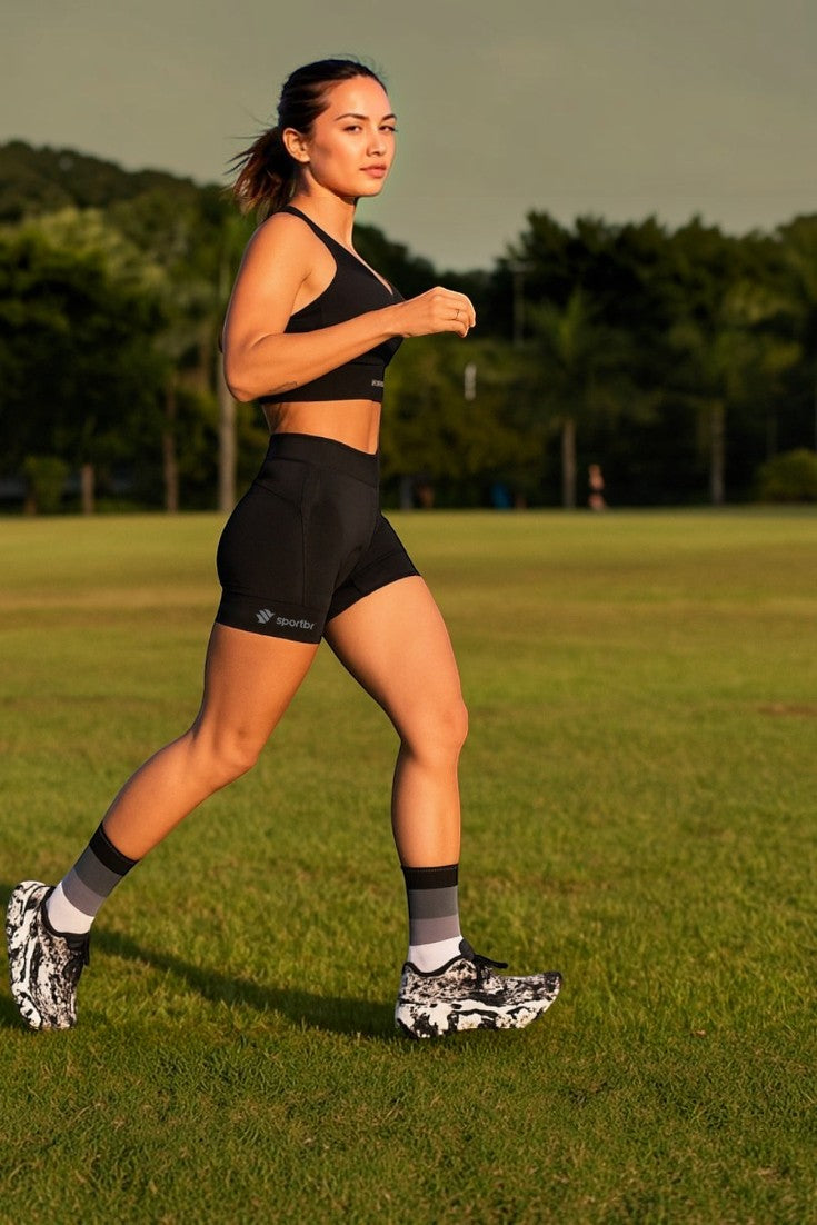 Mulher correndo em campo usando shorts de compressão preto SPORTBR com bolsos laterais e top esportivo combinando