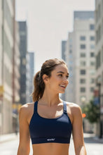 Modelo sorridente usando top esportivo azul marinho de alta sustentação da marca SPORTBR em ambiente urbano.