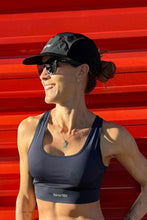 Mulher sorrindo usando top esportivo azul marinho SPORTBR com modelagem nadador, boné preto e óculos de sol.