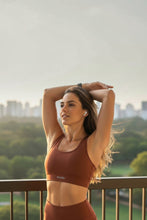 Mulher praticando alongamento ao ar livre usando top esportivo SPORTBR na cor terra cota com design nadador