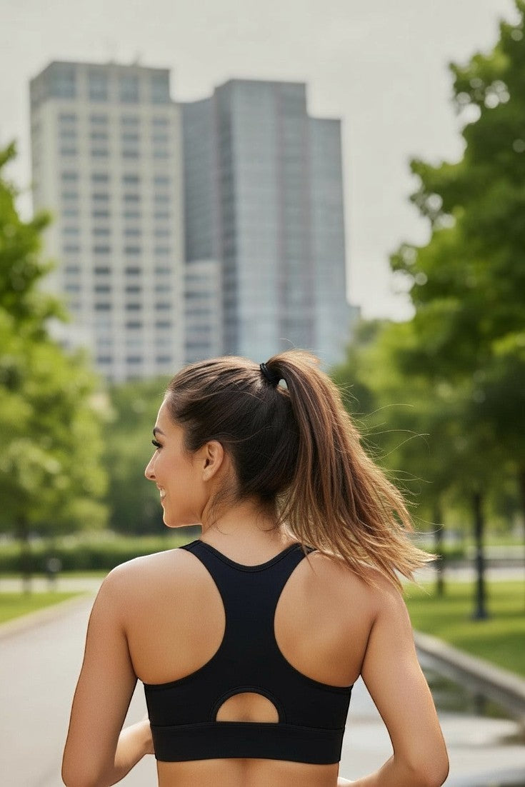 Mulher de costas usando top esportivo preto de alta sustentação SPORTBR com design nadador em parque urbano.