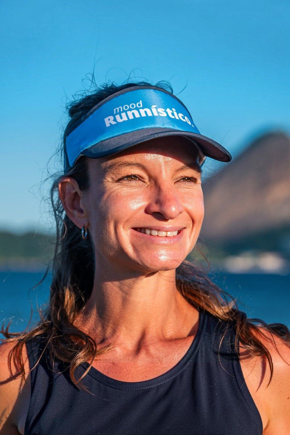 Mulher sorridente usando viseira azul SPORTBR com elástico para corrida ao ar livre sob luz solar