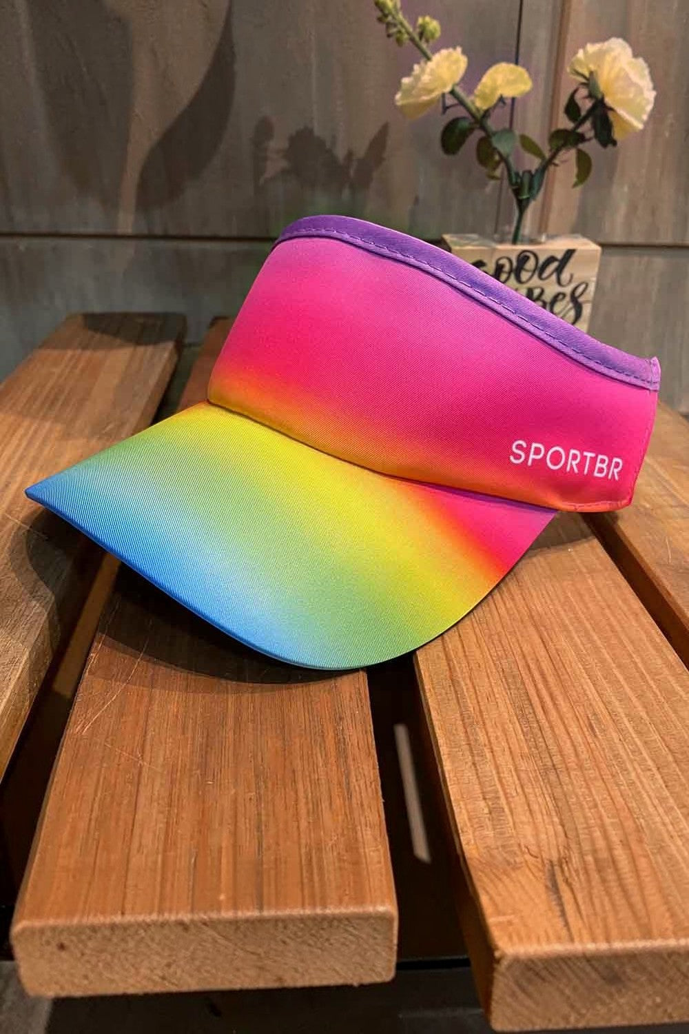 Viseira SPORTBR de corrida com estampa degradê colorida em tons de roxo, rosa, amarelo e azul sobre base de madeira.