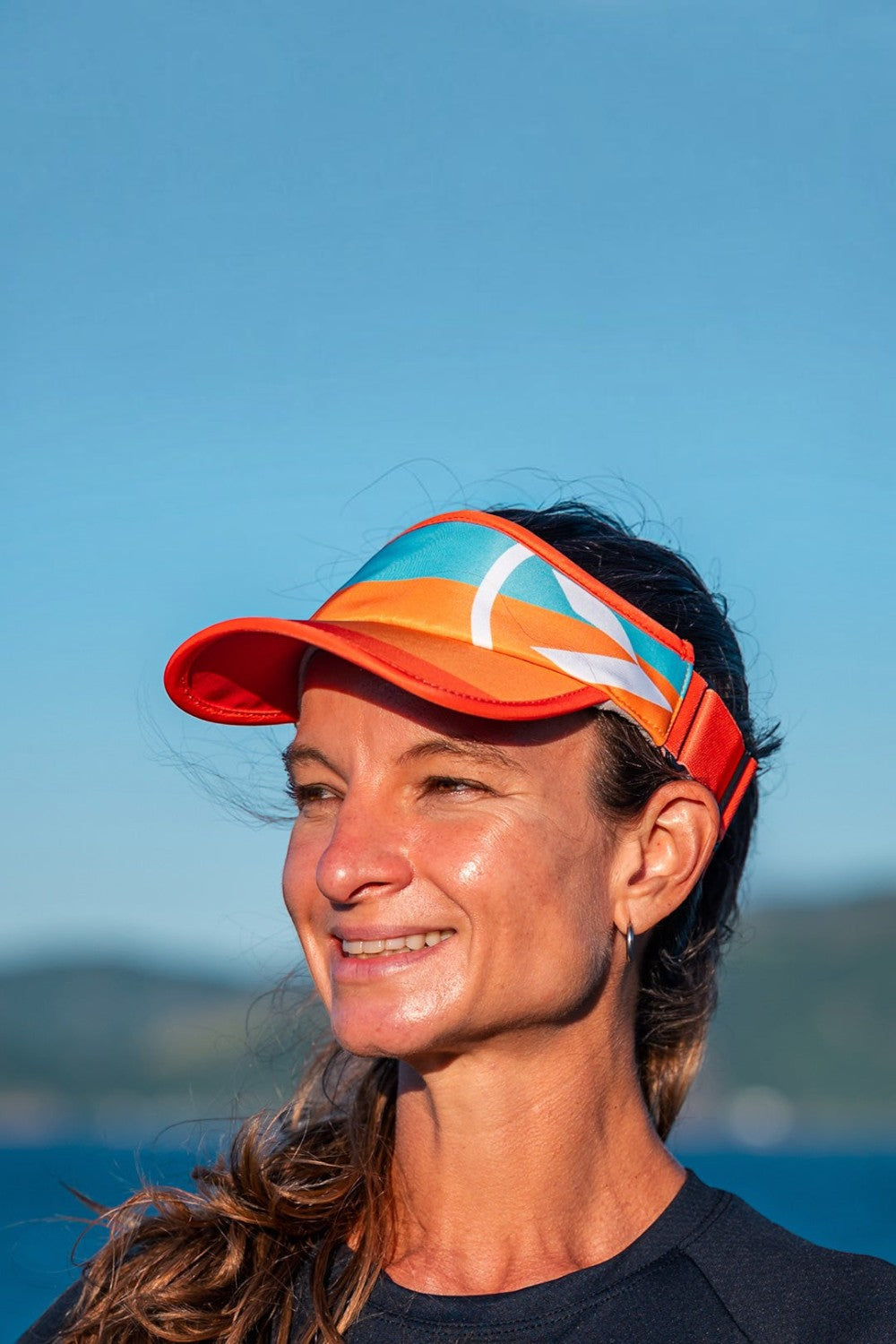 Mulher usando viseira SPORTBR laranja e azul com ajuste elástico durante treino ao ar livre sob céu azul