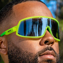 Óculos de sol verde unissex com armação máscara e lente única cinza espelhada, polarizada com proteção UV400. O acessório é leve, confortável e não escorrega ou pula no rosto ao realizar esportes.