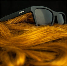 Óculos de sol unissex preto com armação quadrada A Ginger's em foco sob o cabelo ruivo.